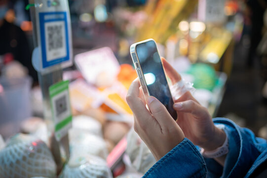 Person using smartphone for QR code payment at night street food market in urban setting