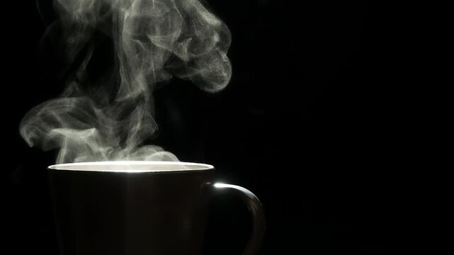 White Steam from the Coffee Mug. A trickle of steam rises and twists gracefully from a cup of hot Coffee. Backlight illuminates brown cup on a black background