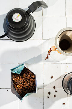Coffee bean in a bag with a pour over coffee pot, grinder and kettle on a white tile surface 