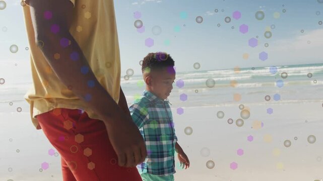 African American man and boy walking shore by waves, in yellow shirt, plaid shirt, bubble overlay