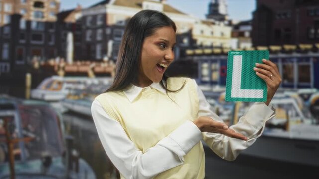 Woman holding green learner l sign with hand on chest in studio while smiling and presenting the plate; pride accomplishment.