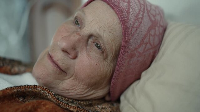 Elderly woman with cancer closing eyes in bed, possibly dying