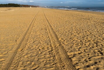 Fresh tire tracks in the sand form striking parallel lines leading into the distance. The light creates strong shadows and textures.
