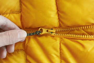 Obraz na płótnie Canvas A hand pulling the zipper of a bright orange puffer jacket. Close up.