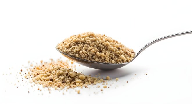 A tablespoon filled with ground hazelnuts, with a small pile spilling over, on a white background, for baking concepts.