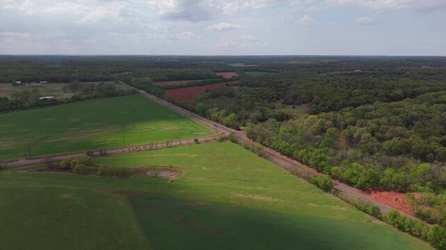 Aerial orbit and tilt down of truck stopping at rural intersection with farmland and patchy sunlight.