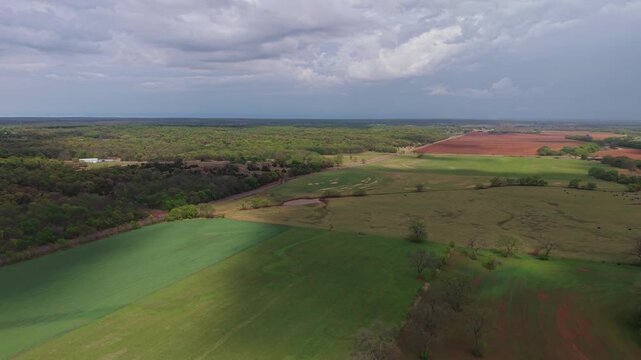 Aerial orbit of cloud shadow moving across farmland fields with patchy sunlight and trees.