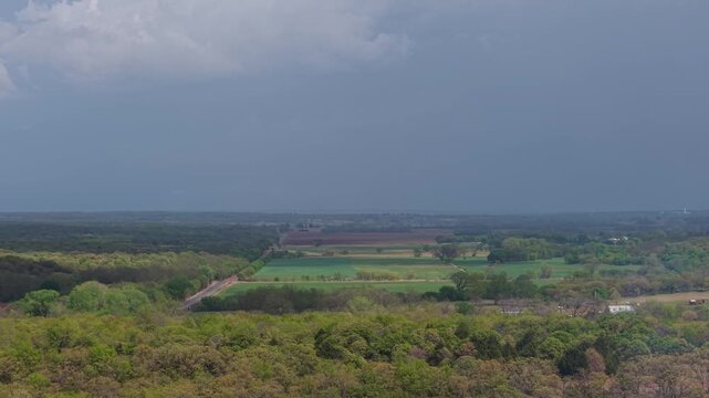 Aerial push toward rain shafts over farmland with patchy sunlight and storm clouds.