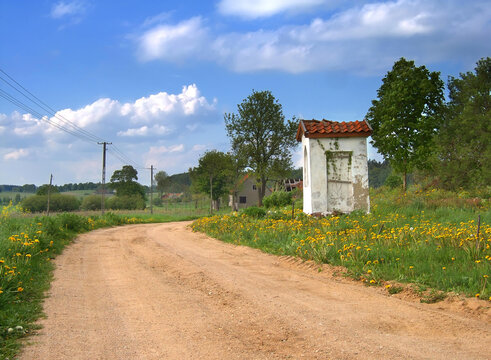 A white roadside chapel in Masuria, Poland. Spring rural landscape with yellow flowers.