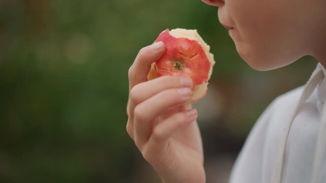 Caucasian child biting ripe apple, lively closeup of lips and hand bringing fruit to mouth backyard orchard vibe with soft bokeh, crisp flesh and audible crunch implied, young gardener and eager