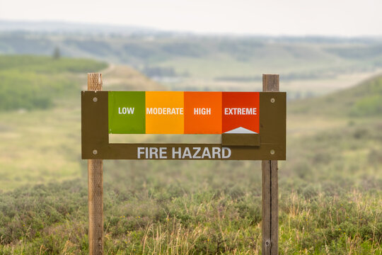 A wooden fire hazard sign indicates an extreme risk level against a blurry rural prairie landscape in Alberta, Canada.