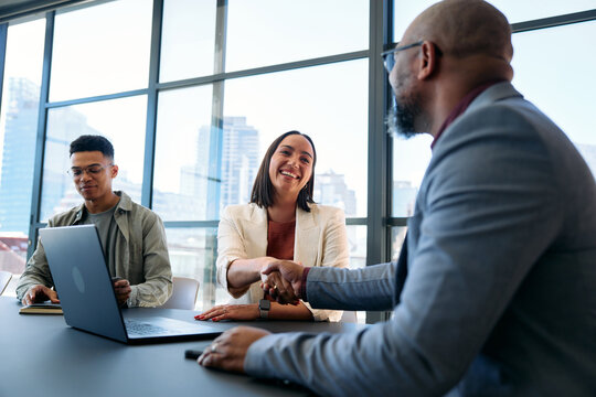 Smiling young businesswoman shaking hands with male colleague in boardroom at office during daytime
