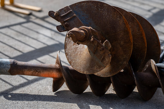 Rusted earth auger drill bit with helical flights and cutting head lying on pavement at a construction site, excavation equipment and ground drilling work