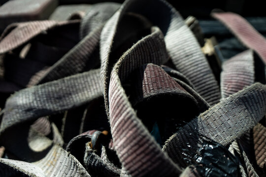 Tangled heavy duty lifting straps and woven webbing slings piled in equipment storage, industrial rigging gear showing wear, reuse and jobsite readiness