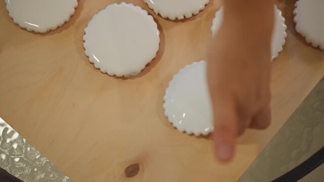 Mini glazed pies on wooden board home baker arranging tartlets while pastry hand picks and inspects edges, creamy white icing, round crusts, warm natural light, cozy kitchen tabletop, rhythmic