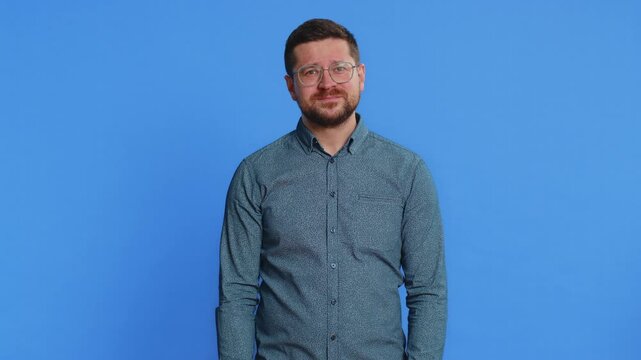 What. Why. Angry confused young man in glasses raising hands in indignant expression, asking reason of failure, demonstrating disbelief irritation by troubles. Guy isolated on blue background