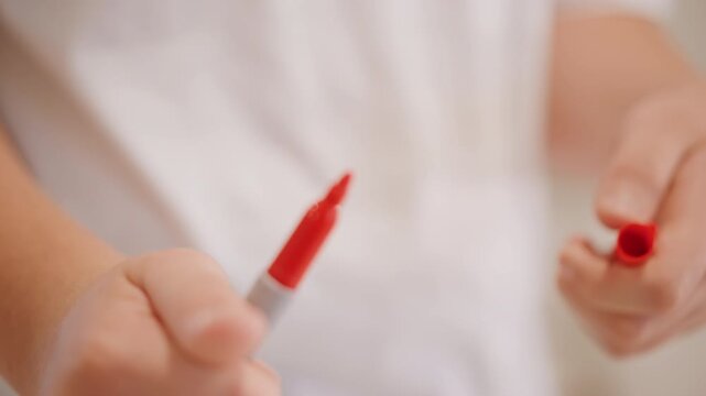 Child hands twisting marker cap closeup, small fingers manipulating plastic cap with rotational pull, tactile focus on grip and motion, casual home lighting, candid study of dexterity before coloring