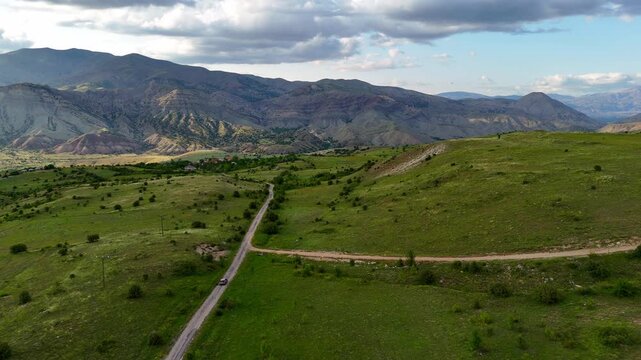 Vehicle travels winding road through. Mountains stretch behind under soft blue sky. Vast landscape offers serene, untouched scenery. Ideal for travel, nature, or adventure-themed projects