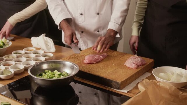 High angle close up shot of unrecognizable male chef in uniform professionally cutting raw chicken breast during cooking master class