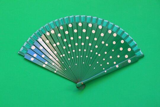 A green hand fan with white polka dots against a matching green background. 