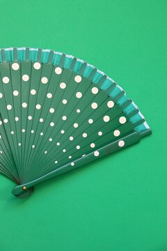 A green hand fan with white polka dots against a matching green background. 