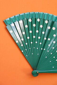 Green hand fan with white polka dots on an orange background. Vibrant color contrast and summer fashion accessory concept.