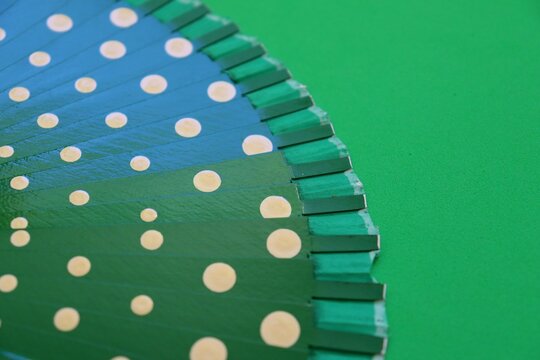 A green hand fan with white polka dots against a matching green background. 