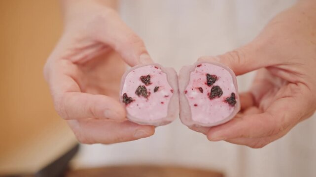Pink treat with fruity core. Pink mochi split open showing rich berry filling and creamy texture. Split pink mochi revealing luscious berry filling held by gentle hands on wooden surface