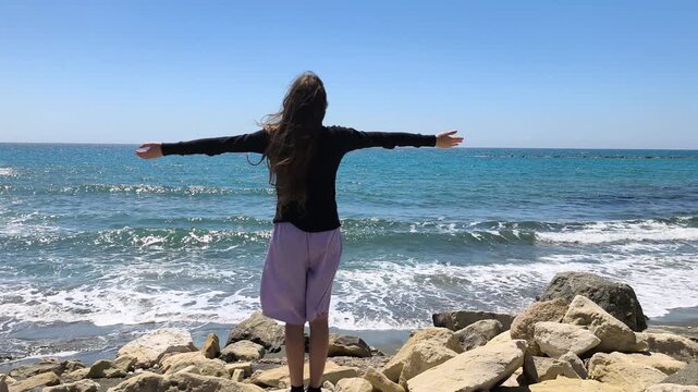 Young Christian Teen Girl Praying Lifting Up Hands of Worship by the Rocky Seashore - Slow Motion Half Speed
