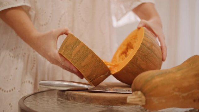 Homemade pumpkin split for pie, hands pulling apart ripe pumpkin on wooden board, visible seeds and bright orange flesh, lace sleeve and warm sunlight, rustic kitchen harvest mood, slow seasonal prep