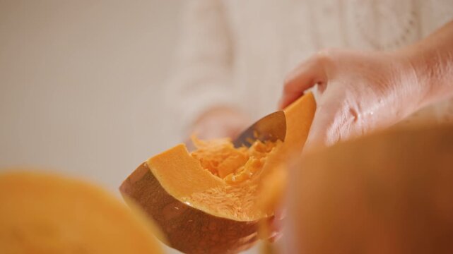 White hands scooping pumpkin pulp soft natural light sweater sleeve careful scraping with spoon into bowl preparing pie filling warm kitchen cozy fall atmosphere tactile orange texture homemade