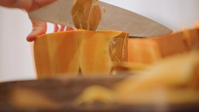 Closeup caucasian hands peeling pumpkin, thin curved slices falling onto wooden board, sharp knife removing rind, bright orange flesh revealed, precise chef movements, modern kitchen lighting, recipe