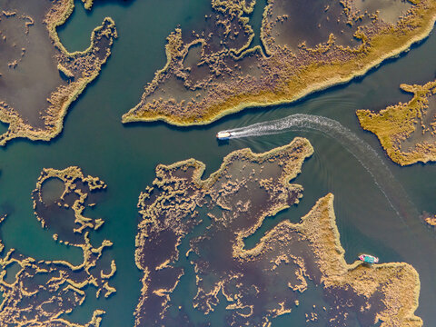 Aerial view of Dalyan River Delta with boats moving through winding channels and wetlands. Natural patterns, marsh ecosystem, tourism activity, water landscape and environmental conservation concept. 