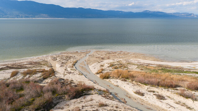 A drone photo of the wide delta and sandy beaches formed where the river flows into the lake, with a mountain backdrop.