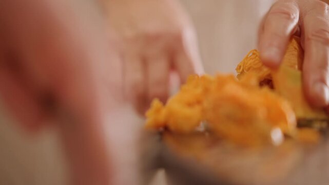 Hands prepare pumpkin. Cooking pumpkin mash attentively. Scooping and shaping pumpkin pulp carefully. Closeup of hands carefully handling pumpkin mash in warm rustic kitchen setting