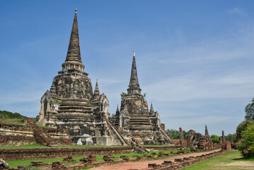 Fototapeta premium Three ancient chedis of Wat Phra Si Sanphet rising behind a red brick wall in golden light at Ayutthaya Historical Park, Thailand.