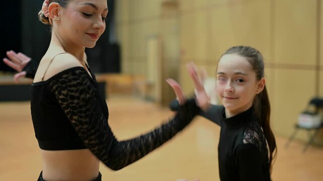 A young female dancer and a girl perform elegant choreography in a dance studio, likely in ballroom or Latin dance style.Both wear black performance outfits that highlight movement and body lines. 