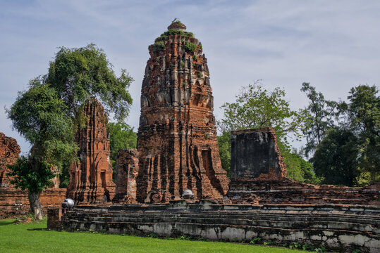 Single ruined prang standing alone on green grass at Ayutthaya, Thailand, under a partly cloudy sky, representing the ancient Siamese kingdom.