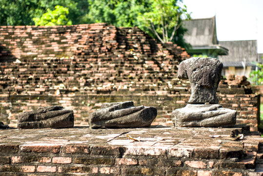Row of headless seated Buddha statues on a green lawn with an ancient brick wall behind at Ayutthaya Historical Park, Thailand.