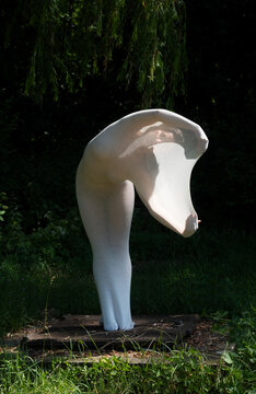 young sexy elegant woman, her body wrapped in long skin tight white dress highlighting body shapes, shone through with sunlight from behind, as living statue on pedestal in nature