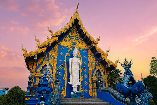 Blue and gold thai temple front with standing buddha statue and carved naga guardians at sunset for travel poster and background design