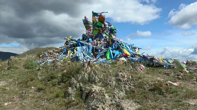 The sacred structure made of stones and logs (ovoo, obo), decorated with multi-colored
scarves and flags fluttering in a strong wind against a picturesque cloudy sky.