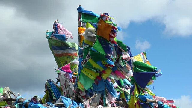 The sacred structure made of stones and logs (ovoo, obo), decorated with multi-colored
scarves and flags fluttering in a strong wind against a picturesque cloudy sky.