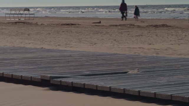 Quiet promenade with footprints and distant waves. Tranquil boardwalk extending to faraway sandy shoreline in winter