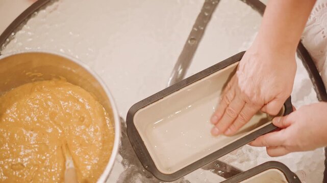 Greasing loaf pan with hand overhead shot of baker pressing butter and flour into ceramic loaf tin, smoothing parchment lining, preparing multiple tins for spiced pumpkin bread, careful prep and neat