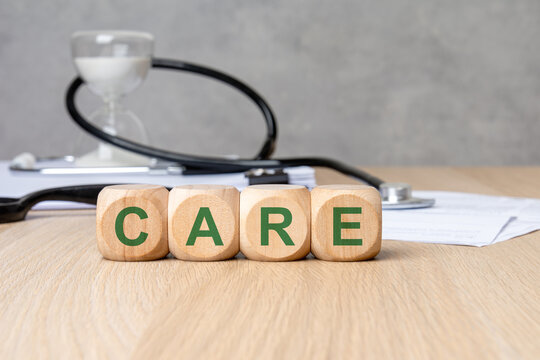 CARE word in green on wooden blocks. Blurred medical background with stethoscope, hourglass and documents. Healthcare concept.