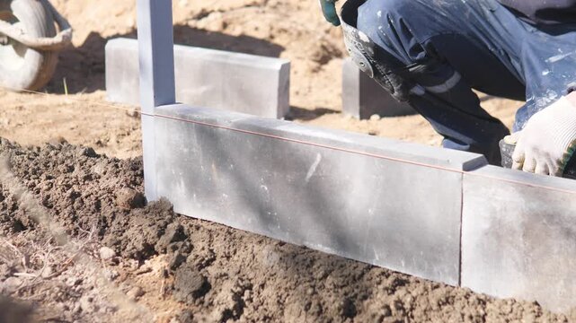 Outdoor Construction Worker Ensuring Proper Wall Placement With Tools. Bright Daytime Environment Where Supervisor Verifies Correctly Aligned Concrete Walls And Associated Equipment