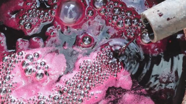 Appetizing freshly squeezed burgundy grape juice flows in a stream into the pan.