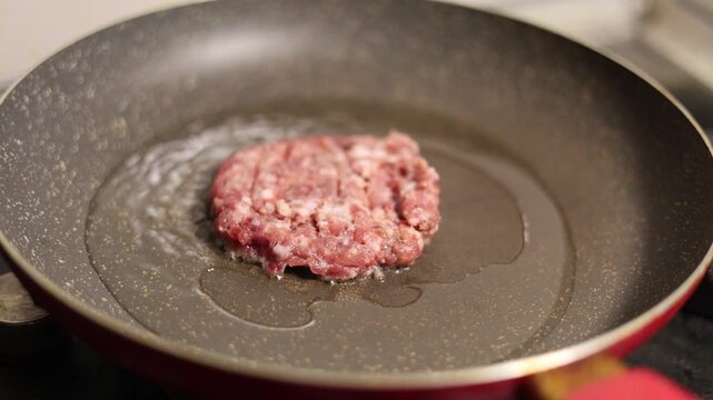 4K video close up. 60 fps. Round burger patty, cutlet of ground beef, vegan meat, pork, lamb is fried in sunflower oil on frying pan with splashes and bubbling on kitchen cafe. Dinner, lunch, dish