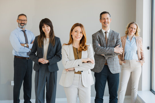 DIverse group of professional business people standing together in a modern office, smiling and posing confidently for the camera.